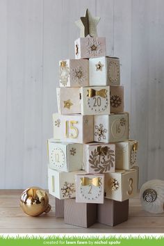 a christmas tree made out of cubes with numbers and ornaments around it on a wooden table