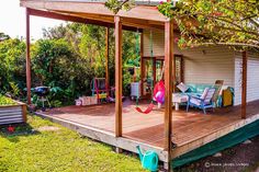 a wooden deck with chairs and umbrellas in the grass next to a small house