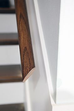 a wooden hand rail on the side of a white wall next to a stair case