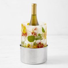 a bottle of wine sitting on top of a metal container filled with leaves and flowers