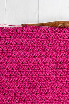 a pink crocheted purse with a wooden handle on a white surface next to a pair of scissors