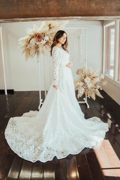 a woman in a white wedding dress standing on a wooden floor next to a flower arrangement