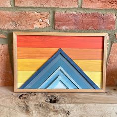 a multicolored wooden frame sitting on top of a wood table next to a brick wall