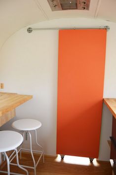 an orange door in the corner of a room with three stools next to it