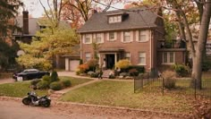 a motorcycle is parked in front of a large brick house with trees and bushes around it