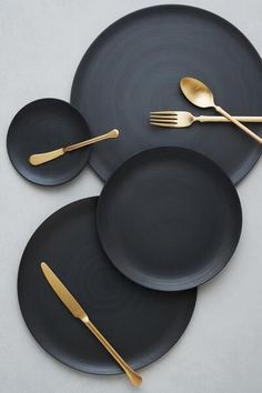 three black plates with gold forks and spoons