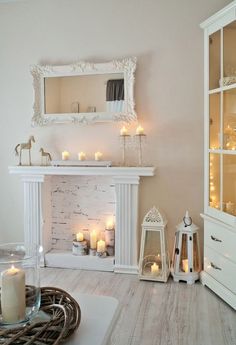 a living room filled with lots of white furniture and candles in front of a fireplace