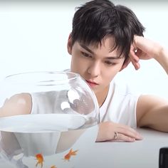 a young man sitting at a table next to a fish bowl with goldfish in it