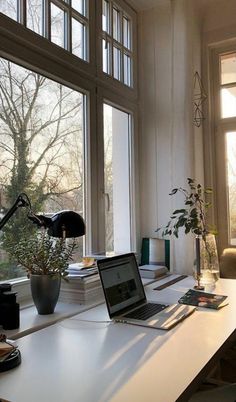 a laptop computer sitting on top of a white desk in front of a large window