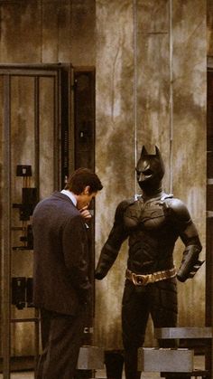 a man in a suit standing next to a batman statue