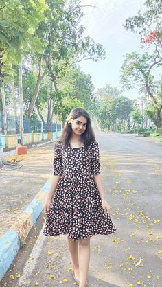 a woman standing in the middle of a road wearing a black and white dress with yellow flowers on it