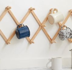 three wooden pegs hold cups and purses on the wall next to a coffee pot