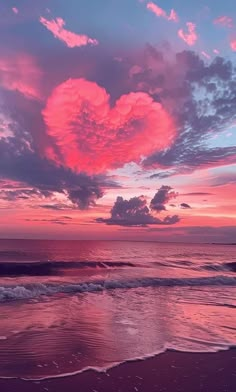 a pink heart shaped cloud hangs over the ocean at sunset with waves lapping in front of it