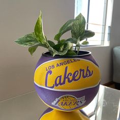 a basketball shaped planter with the los angeles lakers logo on it, sitting on top of a glass table