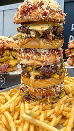 several cheeseburgers stacked on top of each other with french fries in the foreground