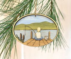 a wooden ornament with a fishing scene on it hanging from a pine tree