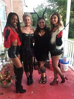 four women dressed up in costumes posing for a photo on the porch with one woman wearing devil horns