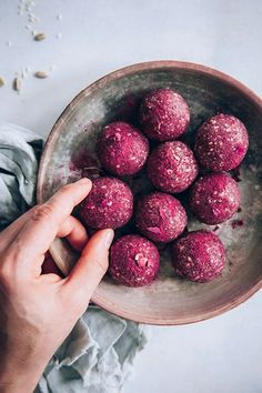 a person is holding a bowl full of pink balls on a white tablecloth with oats scattered around it