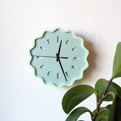 a green clock mounted to the side of a wall next to a potted plant