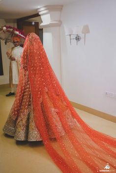 two people standing next to each other in front of a white wall wearing orange and gold outfits