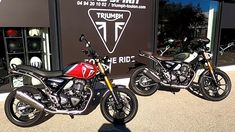 two motorcycles are parked in front of a triumph motorcycle dealership sign and storefront