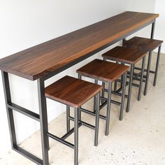 three stools and a long table in a room with white walls on the side