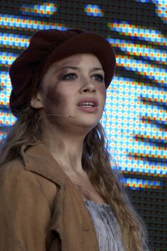 a woman wearing a brown hat standing in front of a colorful screen with dots on it