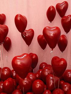 there are many red heart shaped balloons in the shape of hearts hanging from strings on a wall