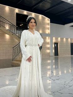 a woman wearing a white gown and tiara standing on a marble floor in front of stairs