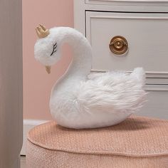 a white swan with a gold crown on its head sitting on a stool in front of a pink wall