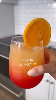 a person holding up a glass with an orange slice in it and the words maibu sunset written on it