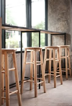 three wooden stools sitting next to each other in front of large windows with barstools