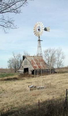 an old barn and windmill in the middle of a field with no leaves on it