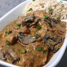 a white plate topped with meat and mushrooms covered in gravy next to rice