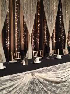 the table is set up with white chairs and black cloth draped over it, surrounded by lights