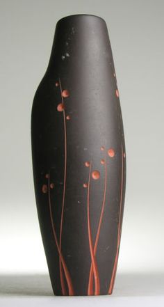 a black vase with red and orange designs on the bottom is sitting in front of a white background