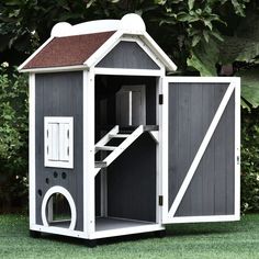 a small dog house made out of wood and painted gray with white trim, sitting in the grass