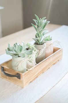 two succulents are sitting in a wooden box on a white tablecloth