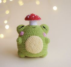 a small crocheted frog with a mushroom on its head sitting in front of some lights