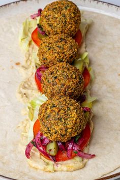 three falafes on top of a tortilla with lettuce and tomatoes