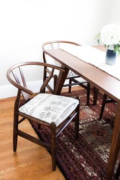 two wooden chairs sitting on top of a rug next to a table with a vase