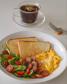 a white plate topped with eggs, toast and salad next to a cup of tea