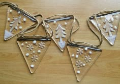 three christmas decorations are hanging from twine on a wooden table with white snowflakes