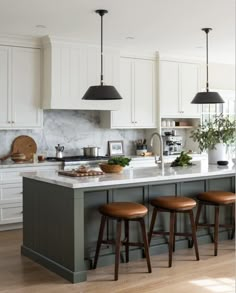 a kitchen island with three stools in front of it and two lights hanging from the ceiling