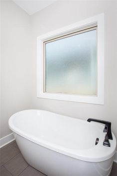 a white bath tub sitting under a window in a bathroom