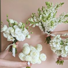 four hands holding white flowers against a pink wall with ribbon around them and tied together