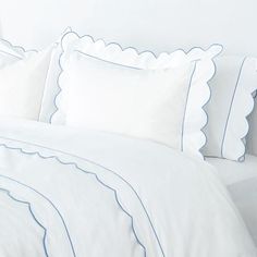 a bed with white sheets and blue scalloped trim on the pillowcases