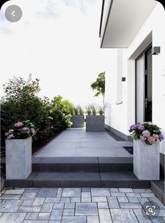 two cement planters sitting on the side of a building next to a sidewalk with flowers in them