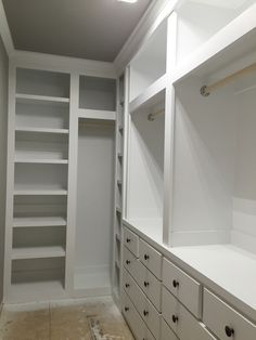 an empty walk in closet with white cabinets and drawers on the wall, next to a light fixture