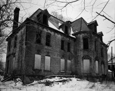 an old abandoned house in the winter with snow on the ground and bare trees around it